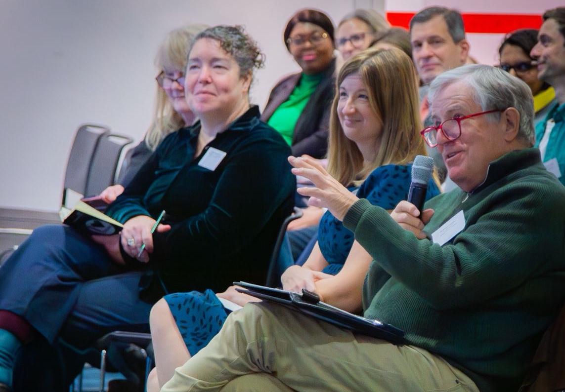 Man seated in the audience of a conference speaking into a microphone